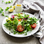Fresh green mixed salad bowl with tomatoes and microgreens on concrete background. Healthy food, top view.